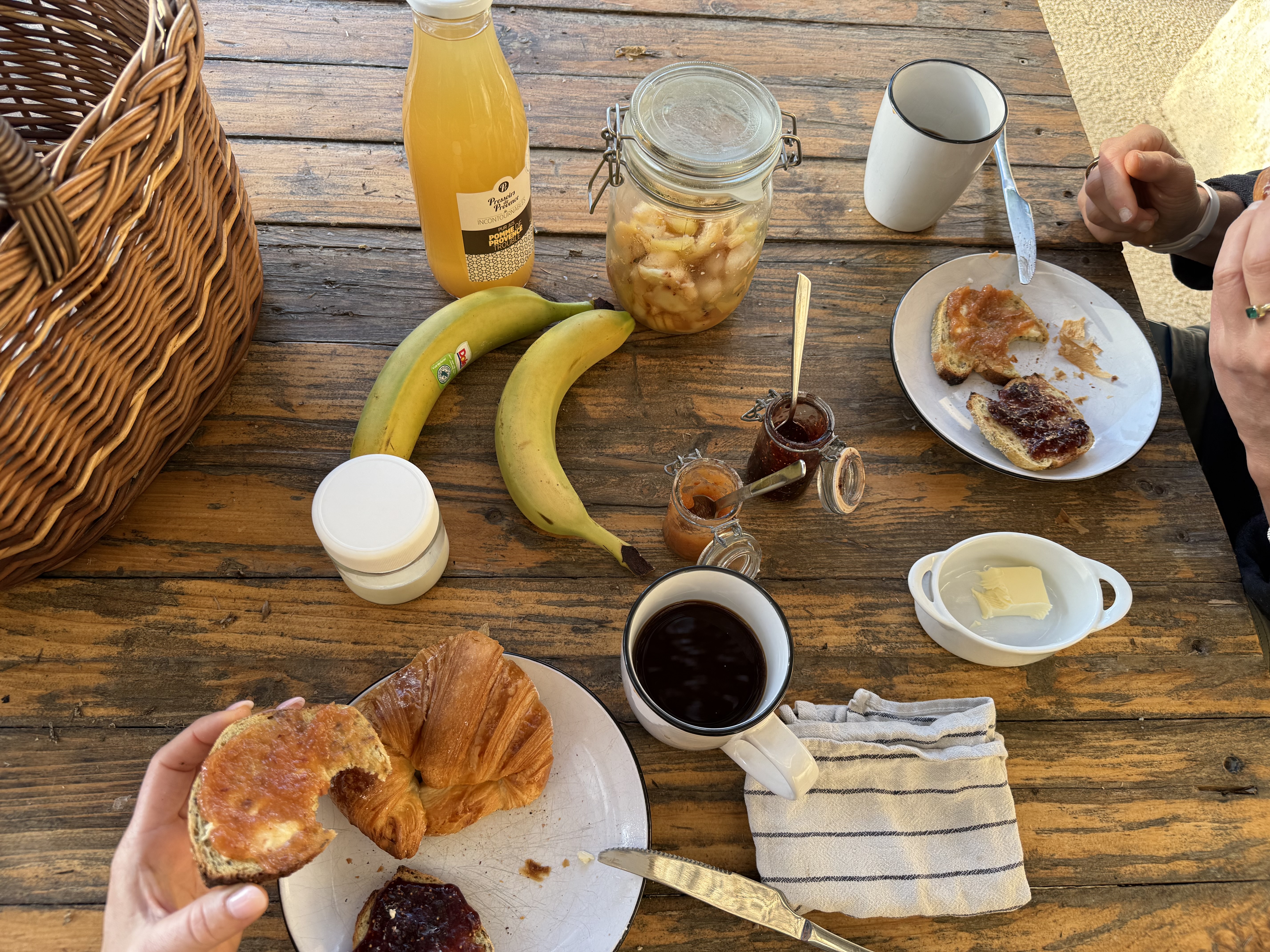 Rustic wooden table set with croissants, jam, bananas, and coffee